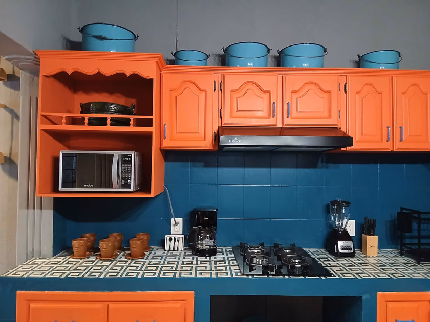 Cocina con alma: Gabinetes en naranja vibrante, muros azul profundo, azulejos de diseño geométrico y ollas de peltre antiguas. Un espacio funcional y moderno que celebra el color, la memoria y las costumbres oaxaqueñas.