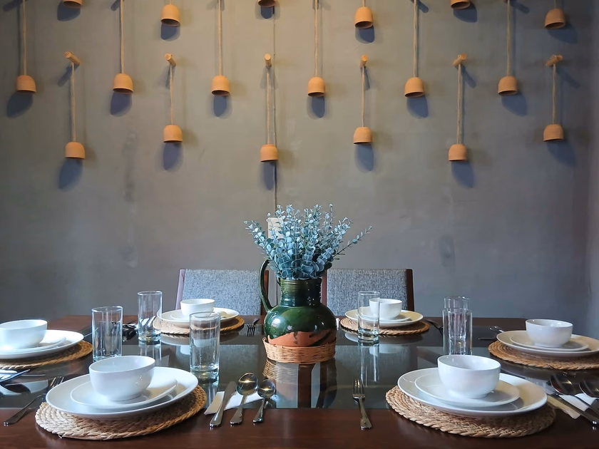 Comedor con detalles únicos: Muro con vasijas de barro suspendidas, mesa recuperada con historia familiar, jarra de barro verde de Atzompa al centro y tapetitos de palma. Un espacio cálido y auténtico para compartir con familiares o amigos.